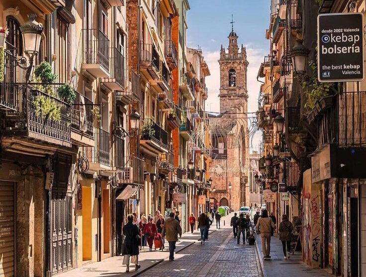 Barrio del Carmen - Valencia Colorful street scene in Barrio del Carmen, Valencia, with people walking and the bell tower of Valencia Cathedral in the background.
